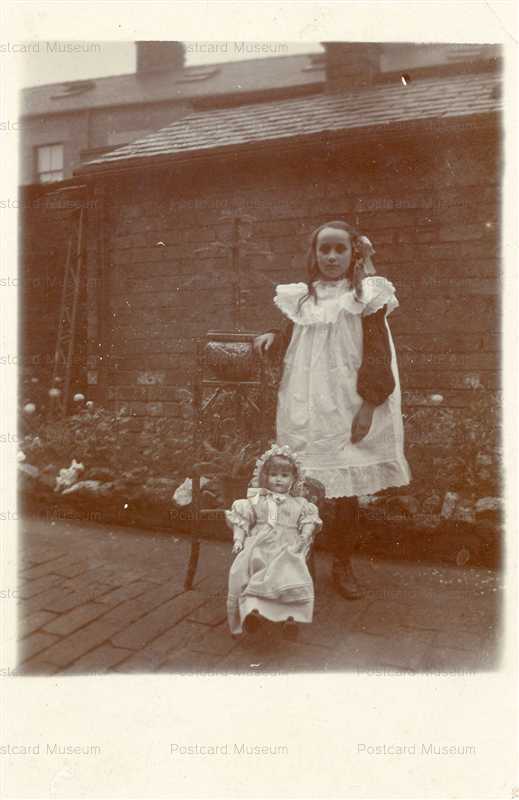 dob340-Girl in Front of a House Standing Next to Her Doll